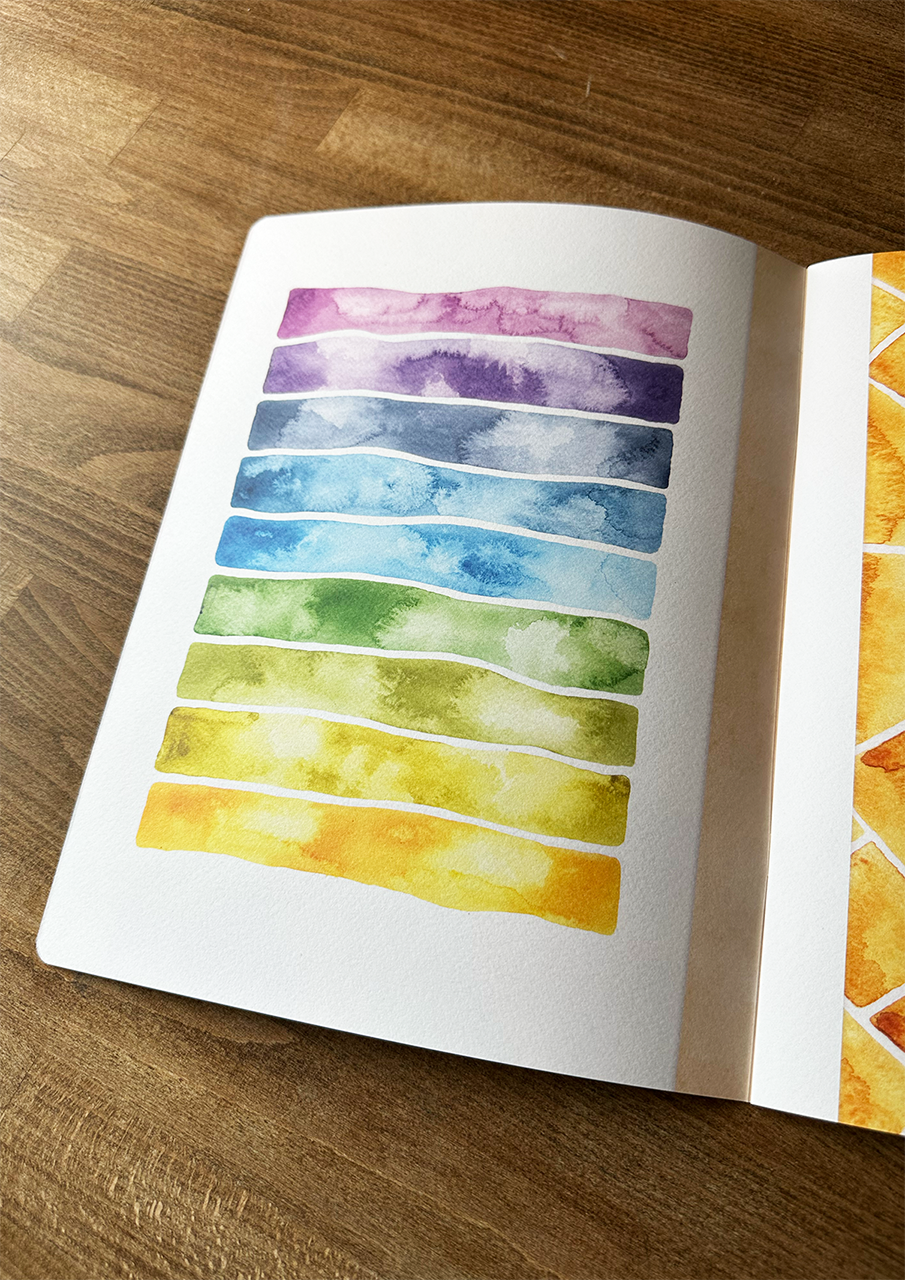 Open book with watercolor swatches on a wooden surface