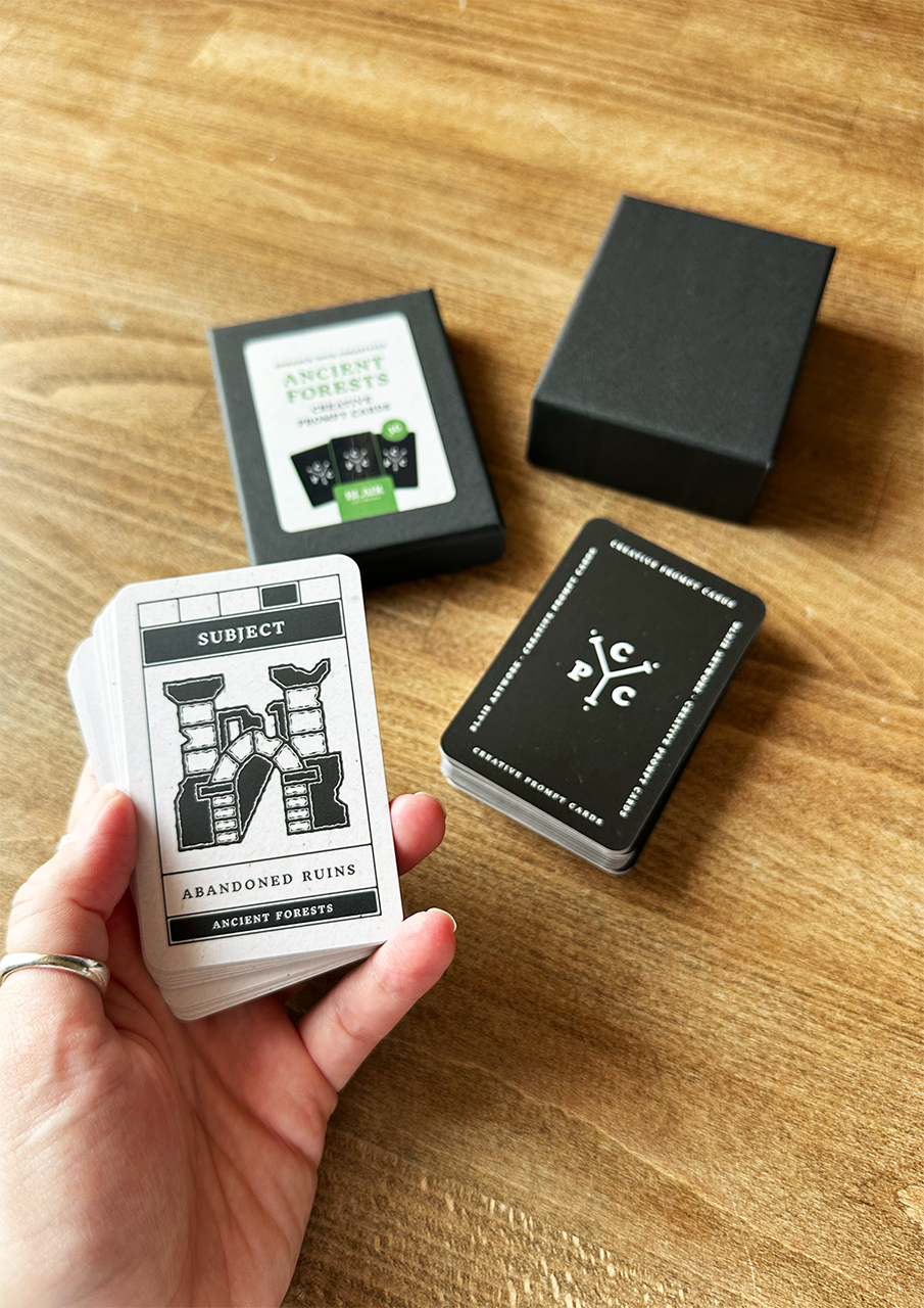 Hand holding a card from a deck with a black box and another card on a wooden surface.