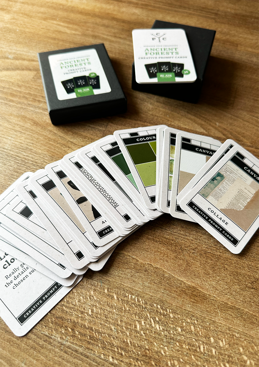 Collection of cards on a wooden surface with two card packs in the background.