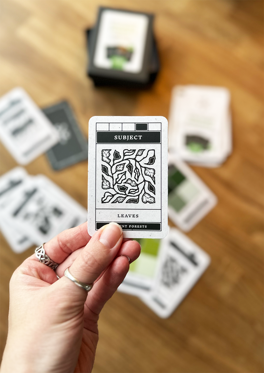 Hand holding a card with 'LEAVES' on it, surrounded by other cards on a wooden surface.