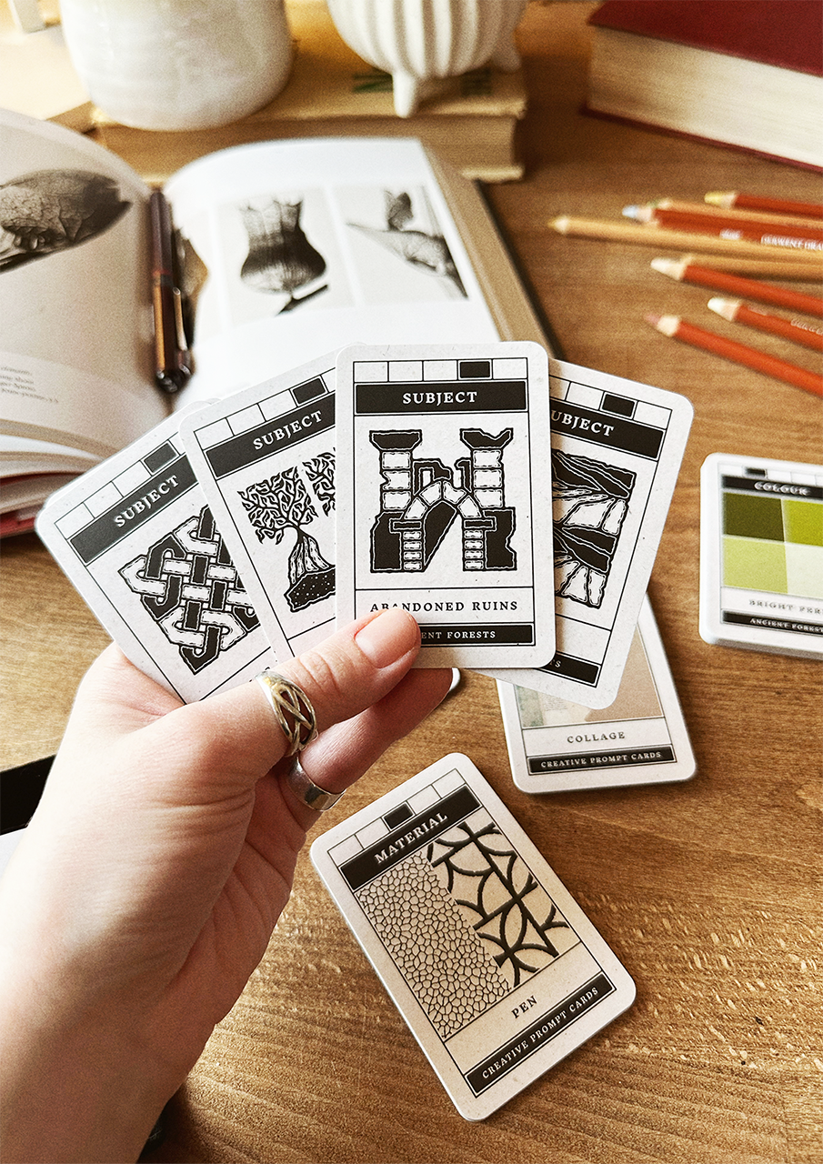 Hand holding a card from a deck of pattern cards on a wooden surface with books and pencils.