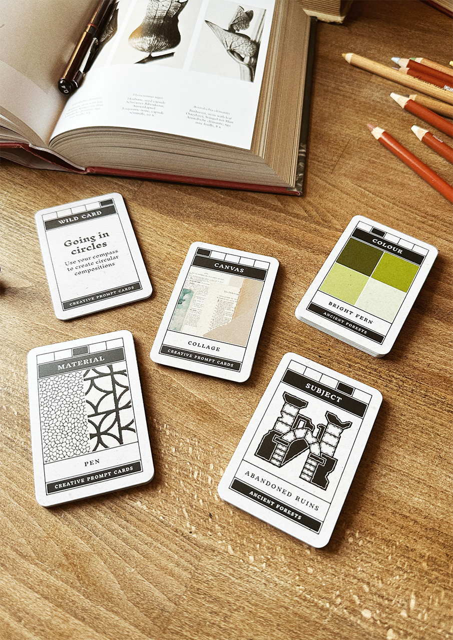 Set of design cards on a wooden surface with an open book and pencils.