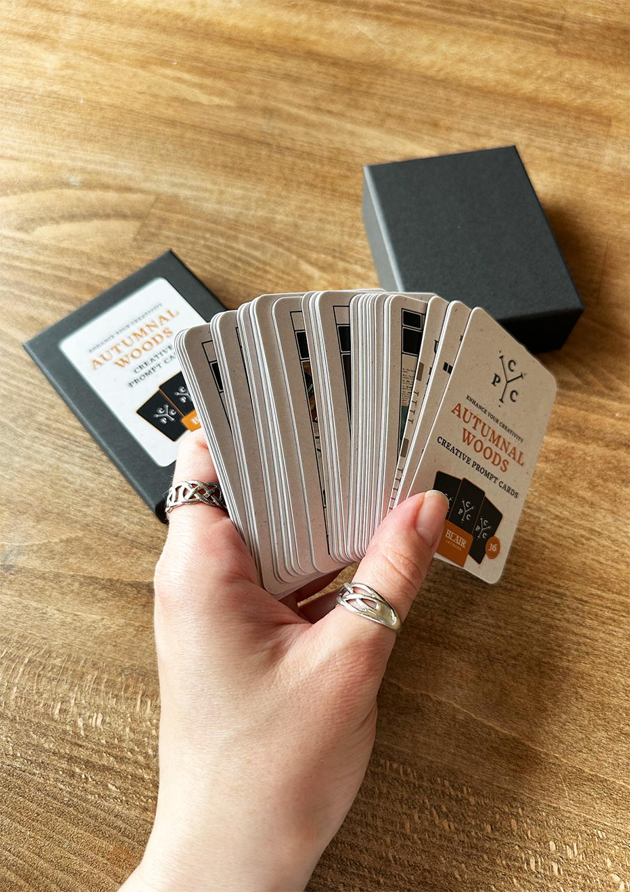 Hand holding a deck of cards on a wooden surface with a card box in the background