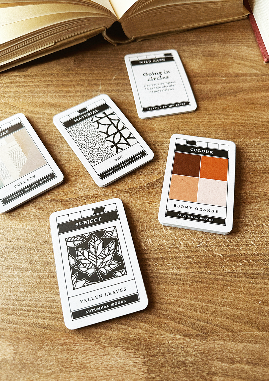 Set of design-themed playing cards on a wooden surface with an open book.