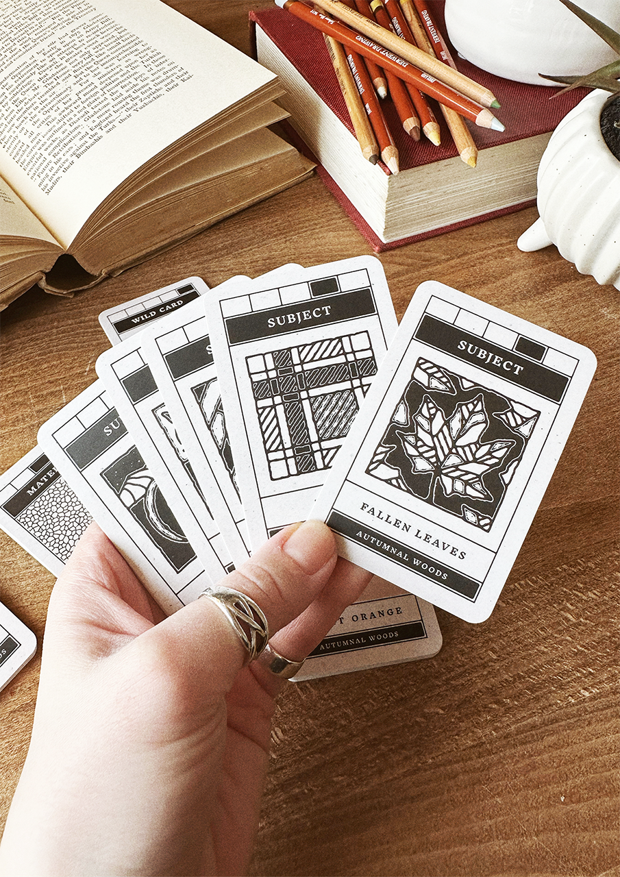 Hand holding patterned cards on a wooden surface with books and pencils in the background