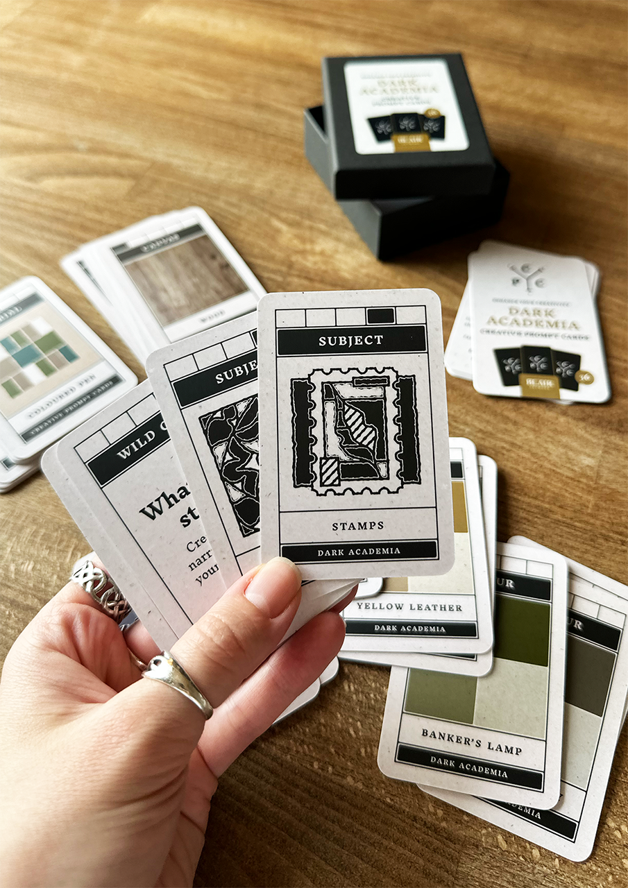 Hand holding a card from a deck of design or art cards on a wooden surface.