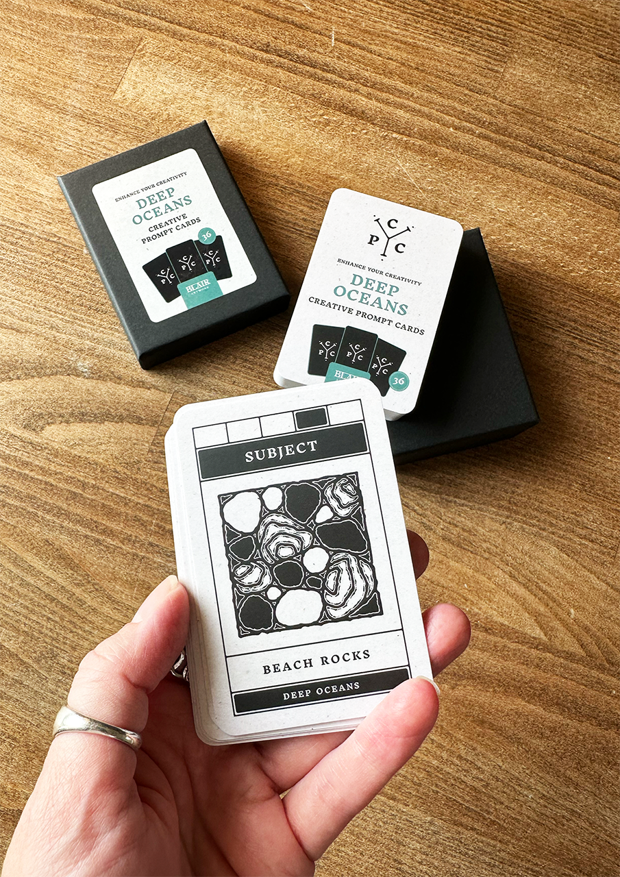 Hand holding a card from 'Deep Oceans' creative deck on a wooden surface