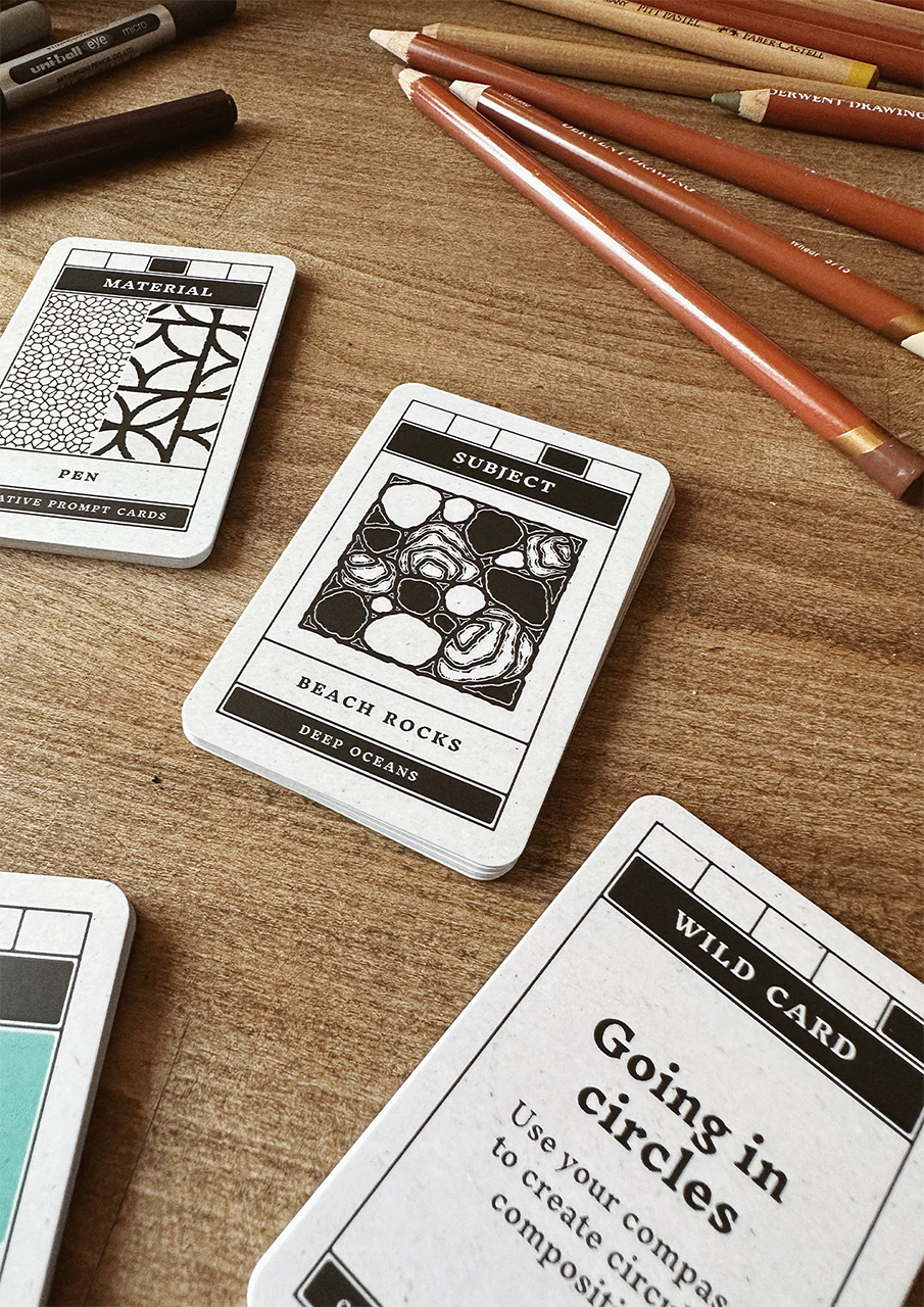 Playing cards with nature-themed designs on a wooden surface with colored pencils.