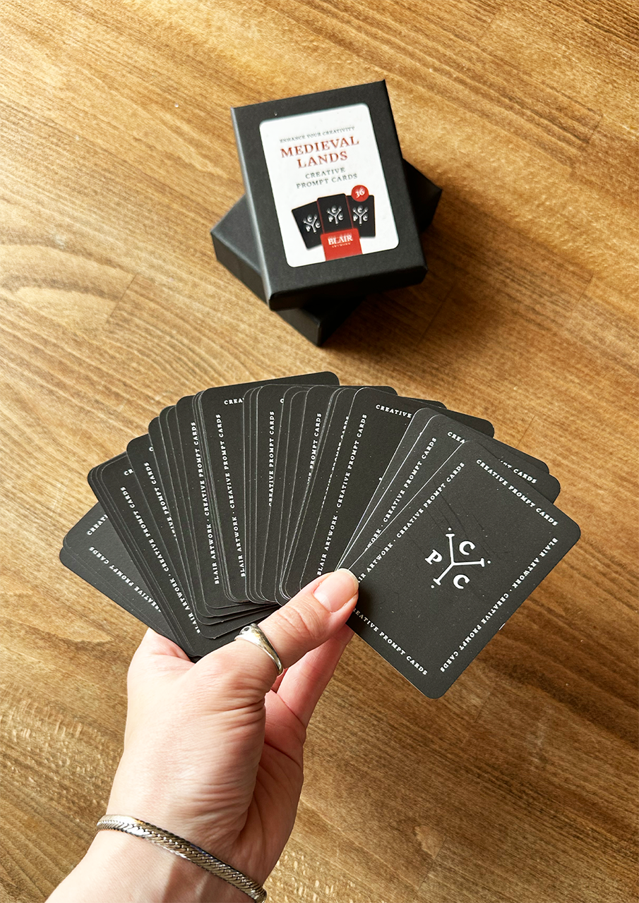 Hand holding playing cards with a deck of cards and box on a wooden surface