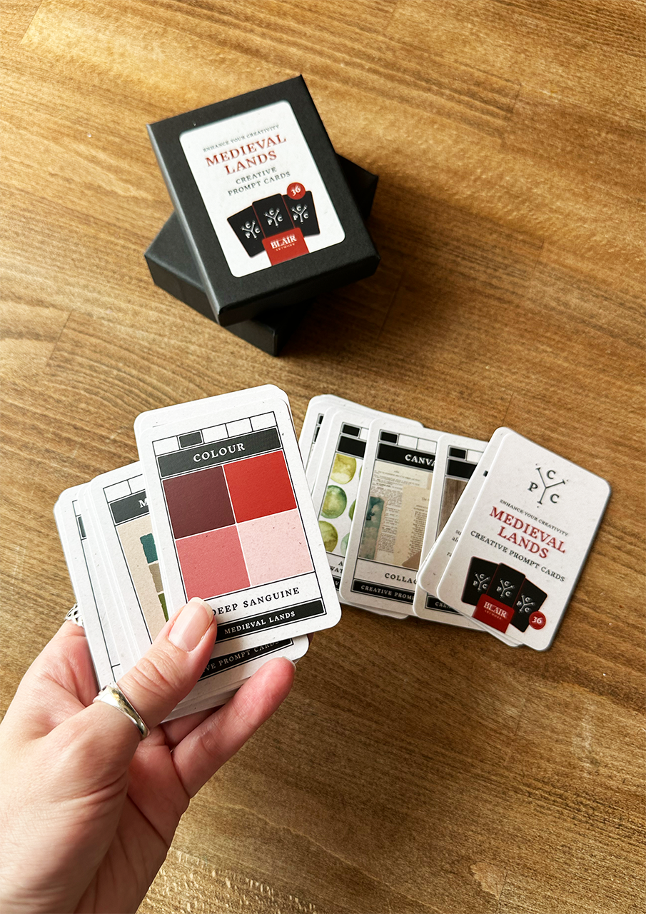 Hand holding playing cards with 'Medieval Lands' box on a wooden surface
