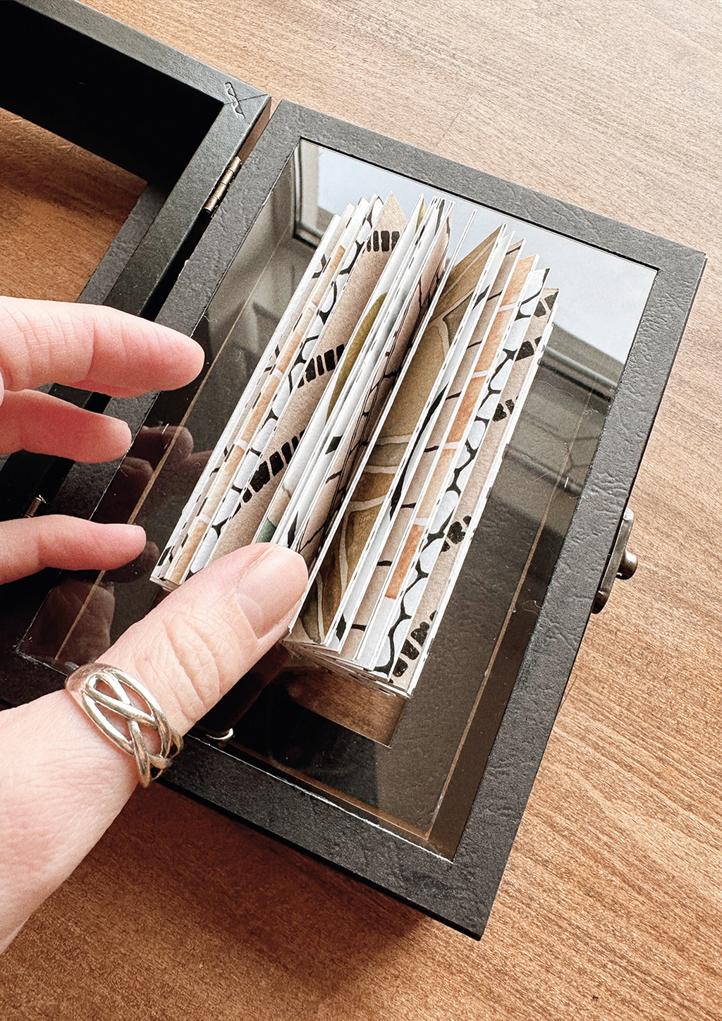 Hand holding artwork in box on wooden surface