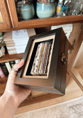 Hand holding artwork in box in front of bookcase