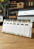 A desktop weekly planner with a watercolor design, displayed on a wooden surface.