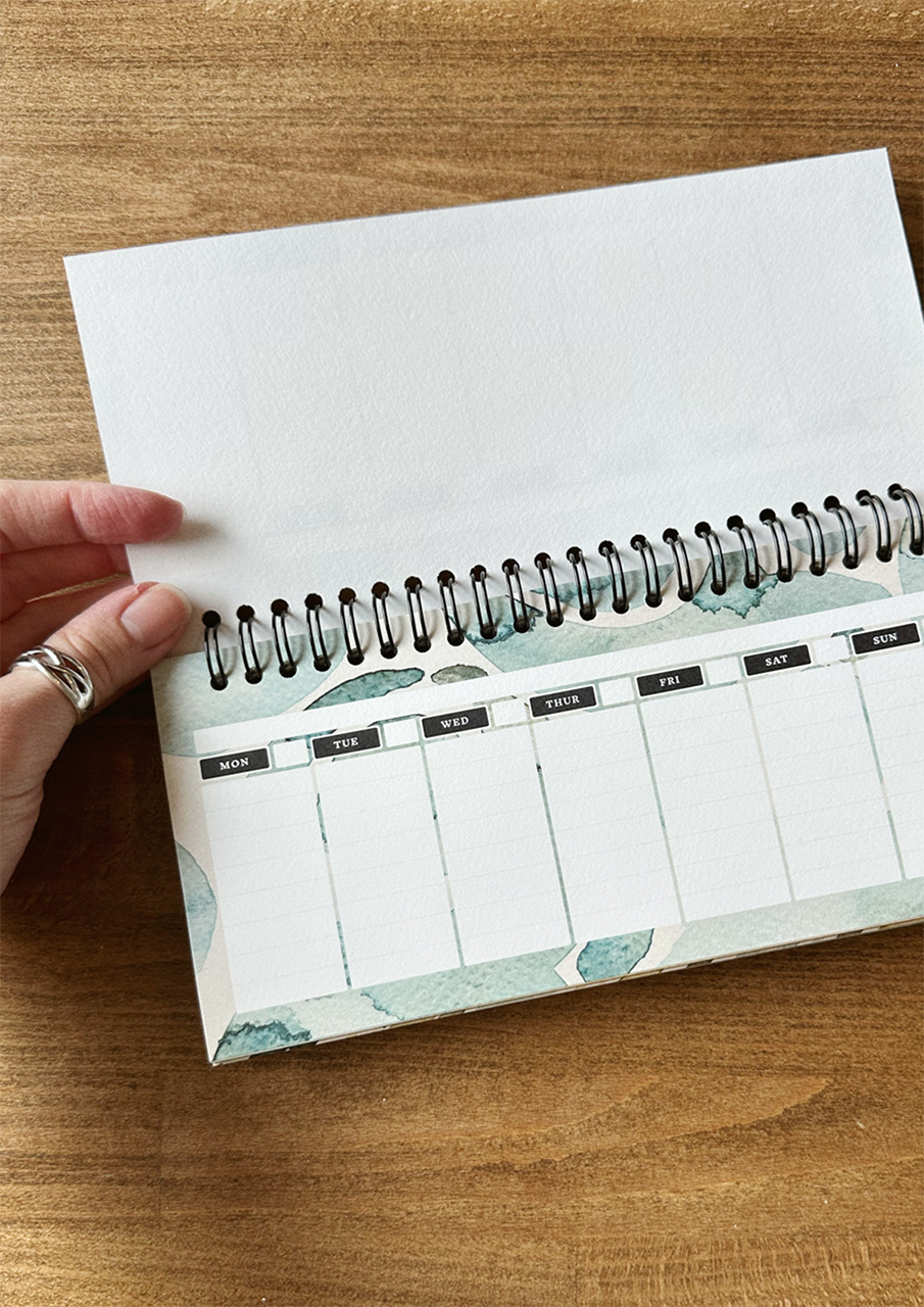 A desktop weekly planner, displayed on a wooden surface.