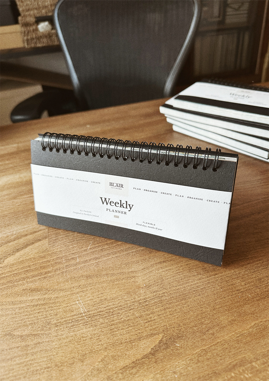 A desktop weekly planner, displayed on a wooden surface.