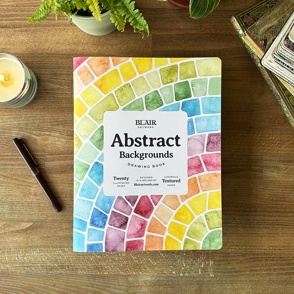 Colorful abstract design notebook on a wooden surface with a candle and pen.