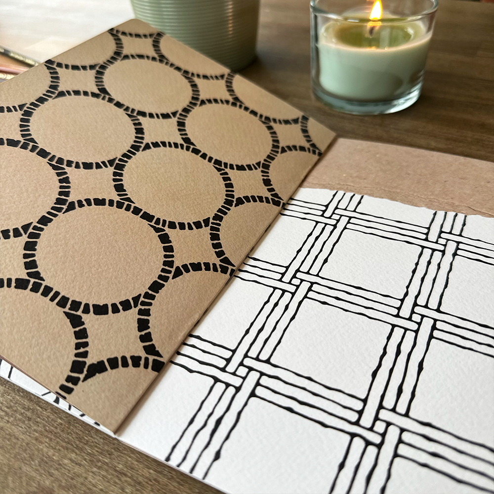 Two patterned pages on a wooden surface with a candle in the background.