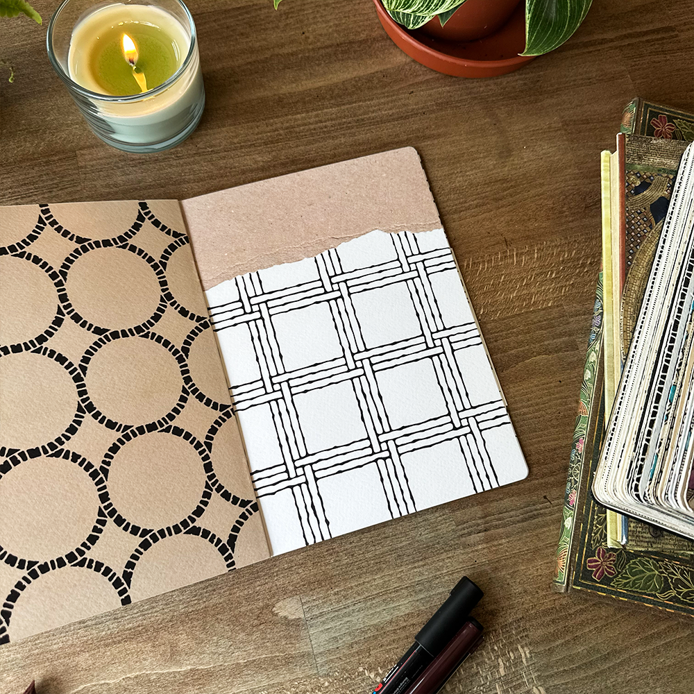 Notebook with patterned pages on a wooden table with a candle and books.