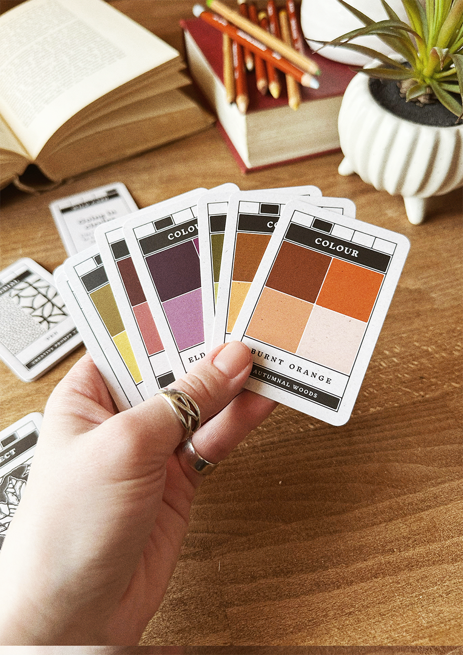 Autumnal Woods CPCs spread out in hand showing coloured prompt cards with books, plants and pencils in the background