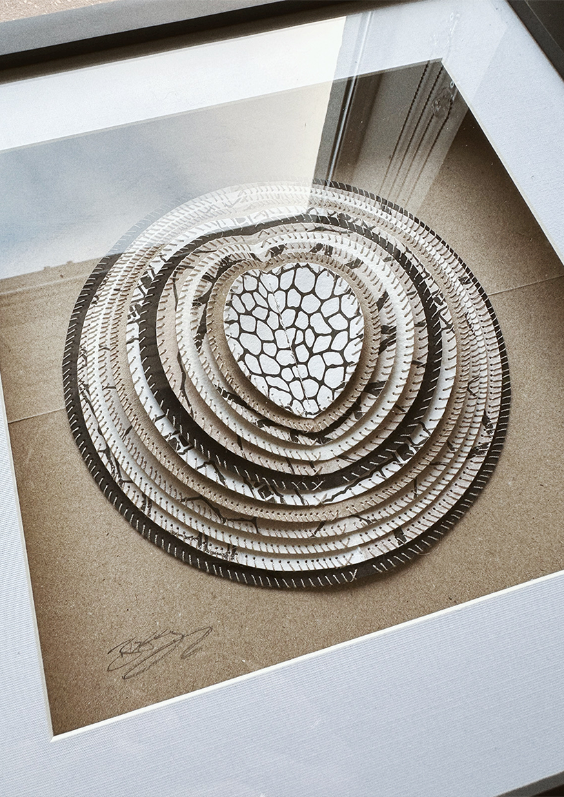 A framed hand-stitched artwork depicting a large circular paper moon in a simple black frame, set against a wooden table and decorative background.