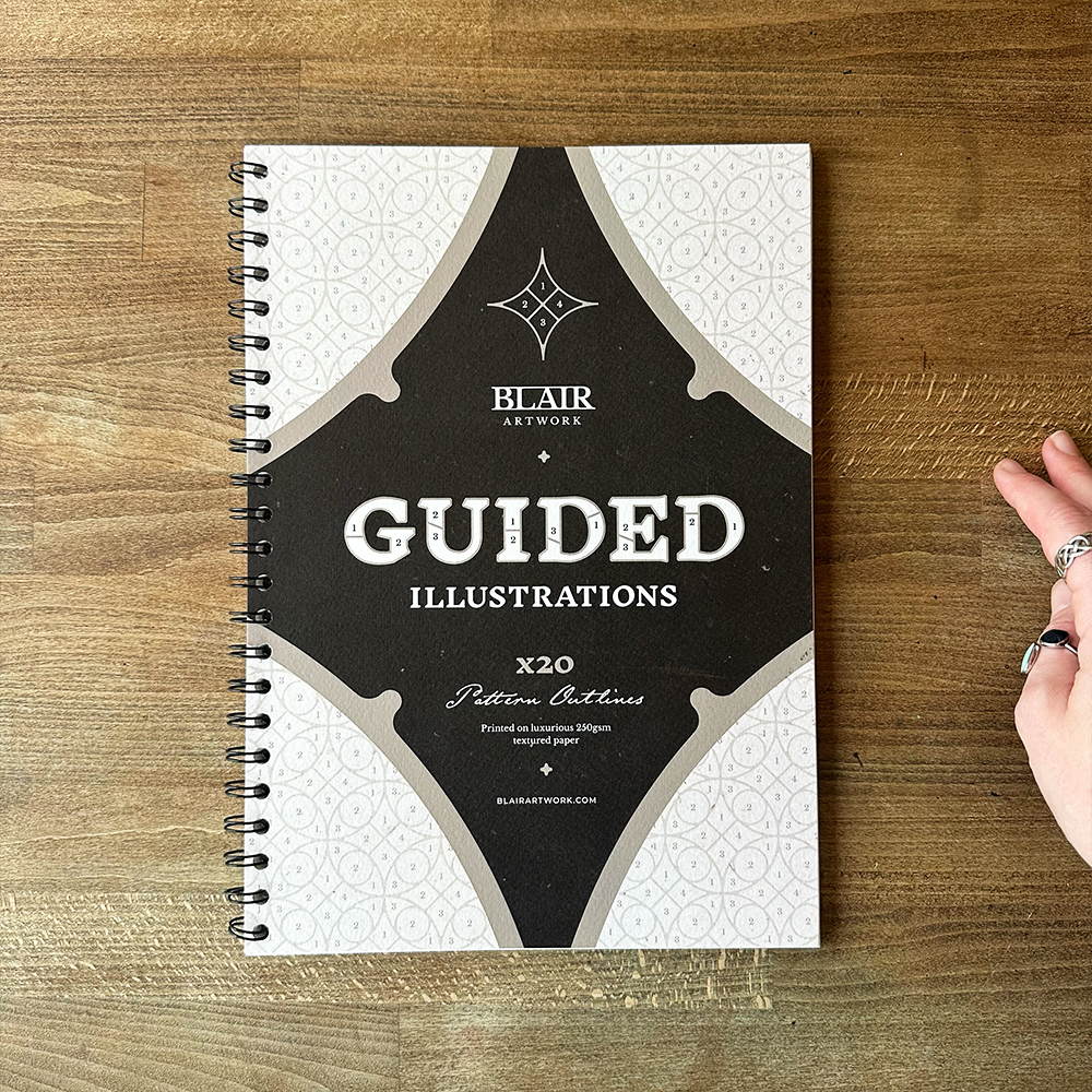 Spiral-bound notebook titled 'Guided Illustrations' by Blair Artwork on a wooden surface.
