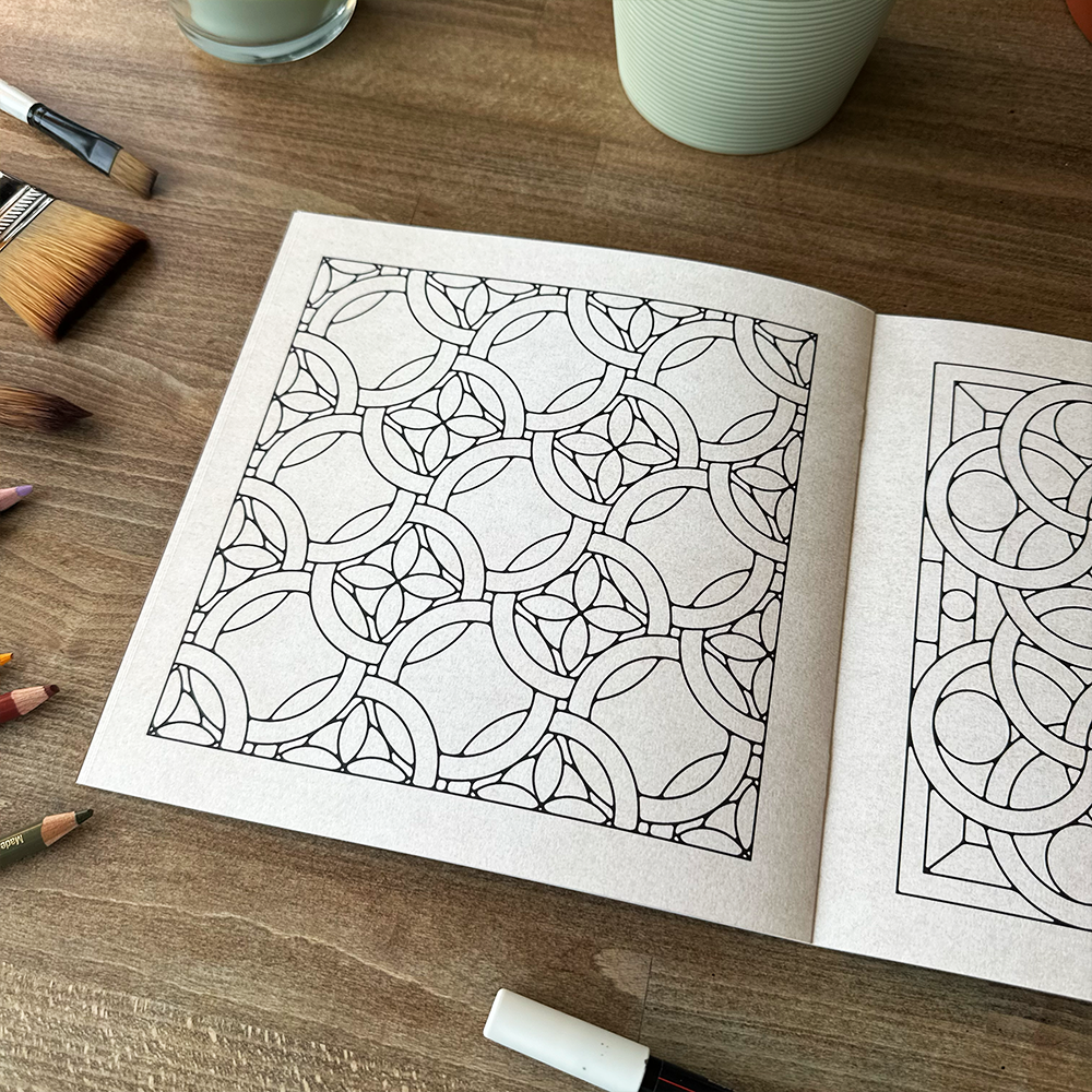 Open book with geometric pattern on a wooden table with art supplies.