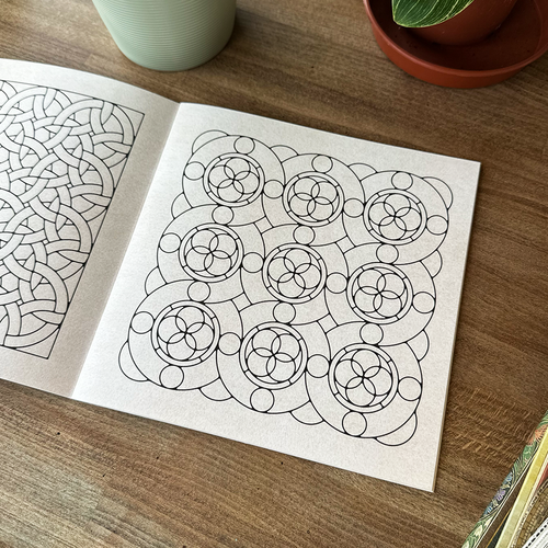 Two sheets of paper with intricate geometric patterns on a wooden surface.