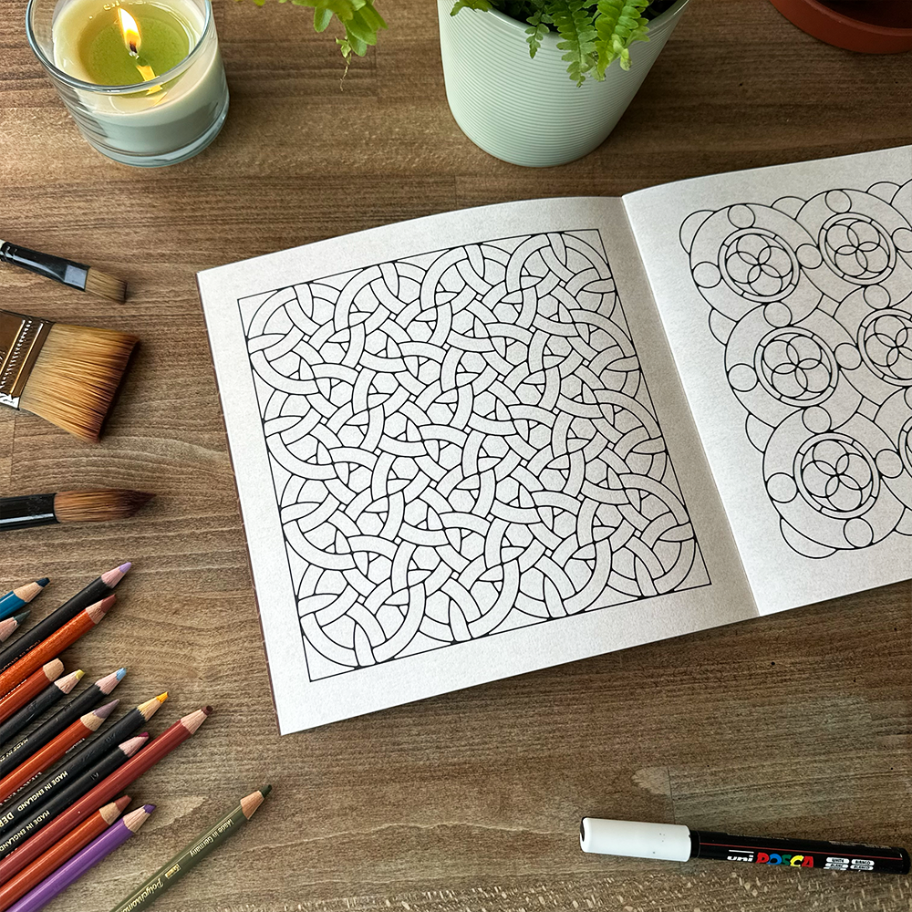 Coloring book with intricate patterns on a wooden table with art supplies.