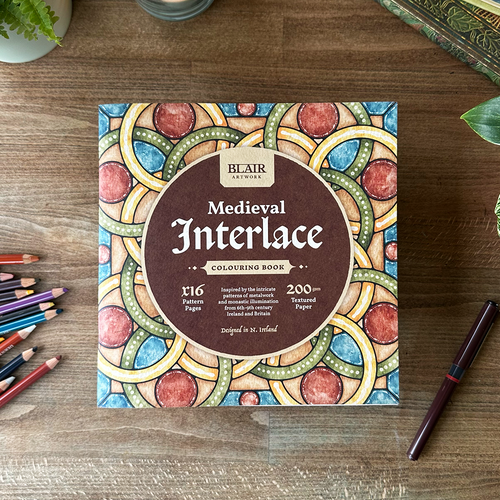 Bear Art Medieval Interlace coloring book on a wooden surface with colored pencils and a pen.