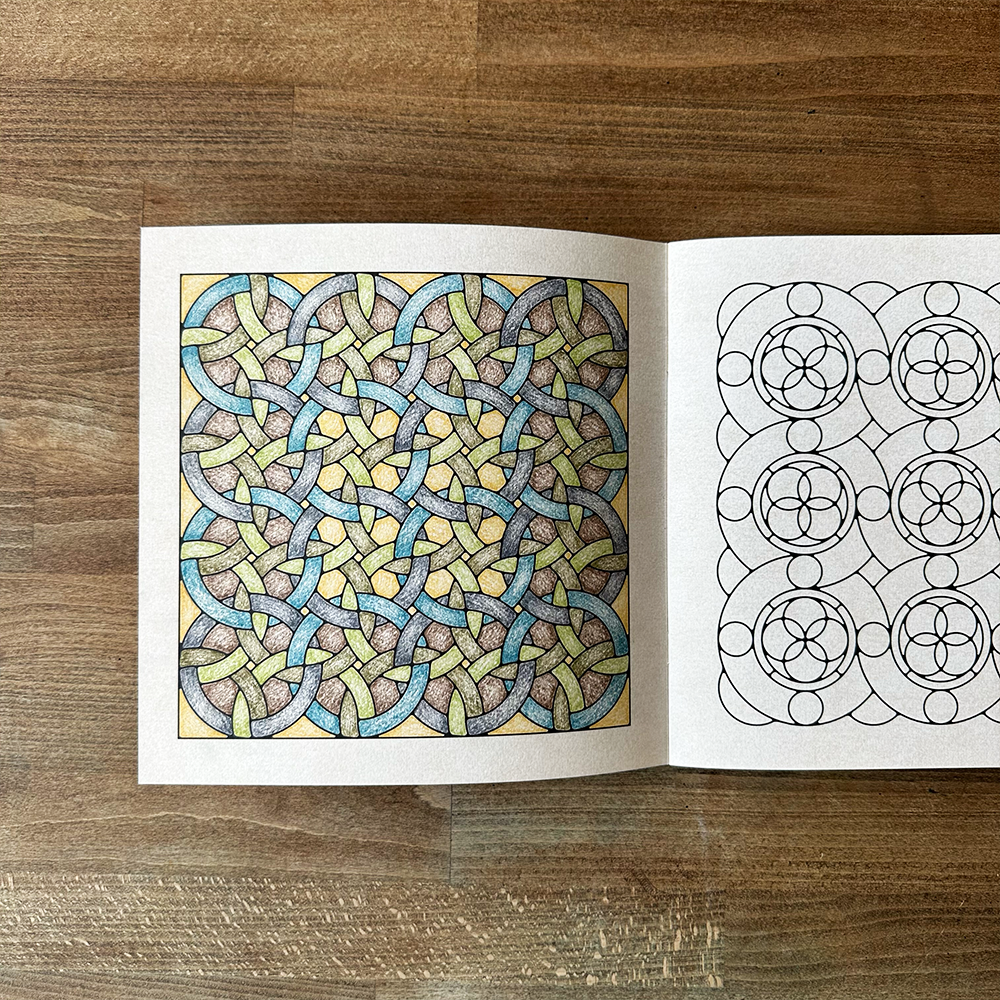 Open coloring book with a completed and an empty design on a wooden surface