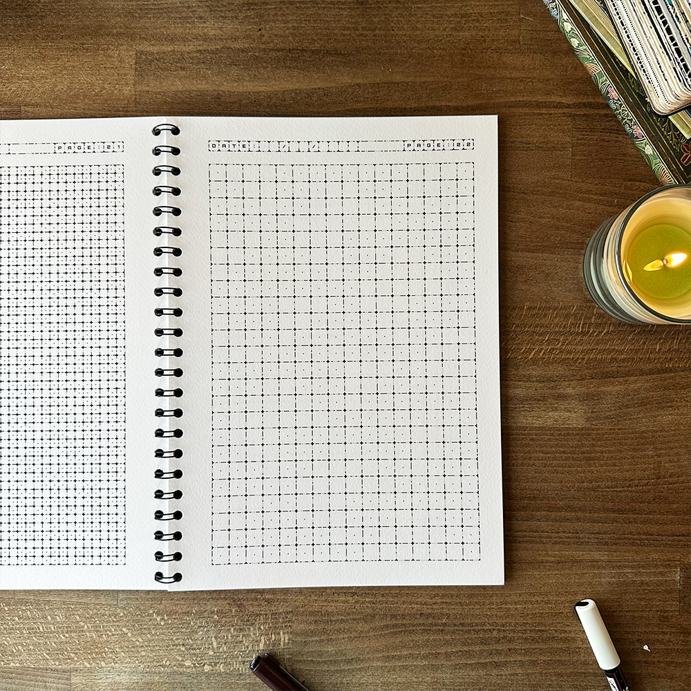 Open notebook with grid pages on a wooden surface next to a lit candle