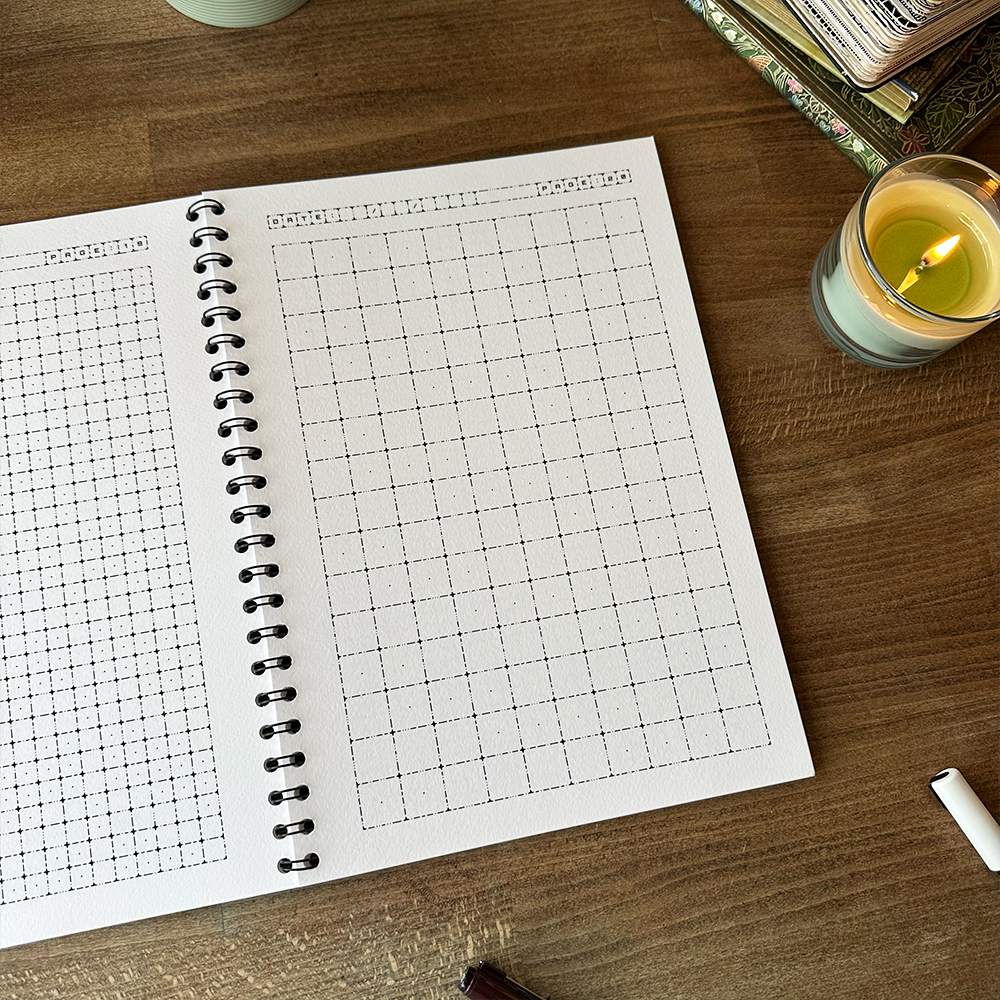 Spiral-bound notebook with grid pages on a wooden surface with a candle and pen.