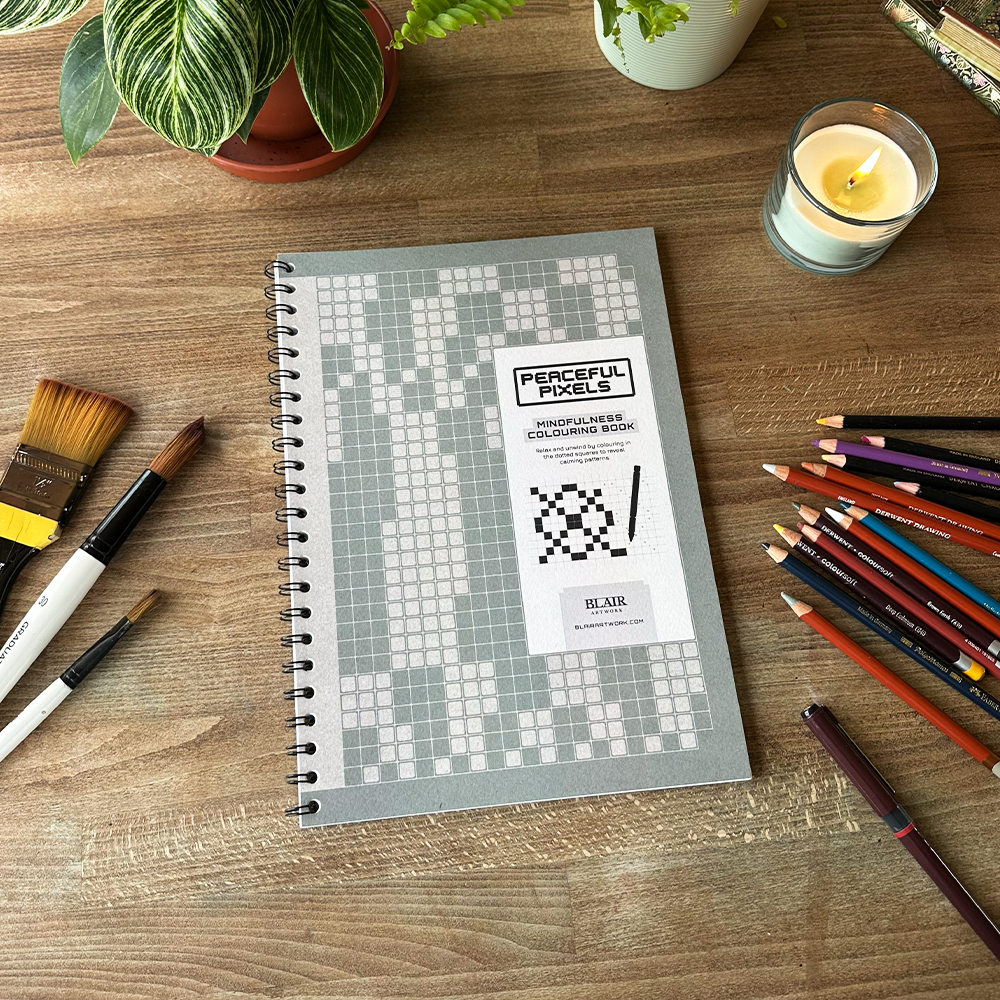 Notebook with 'Peaceful Pixels' on a wooden table with art supplies