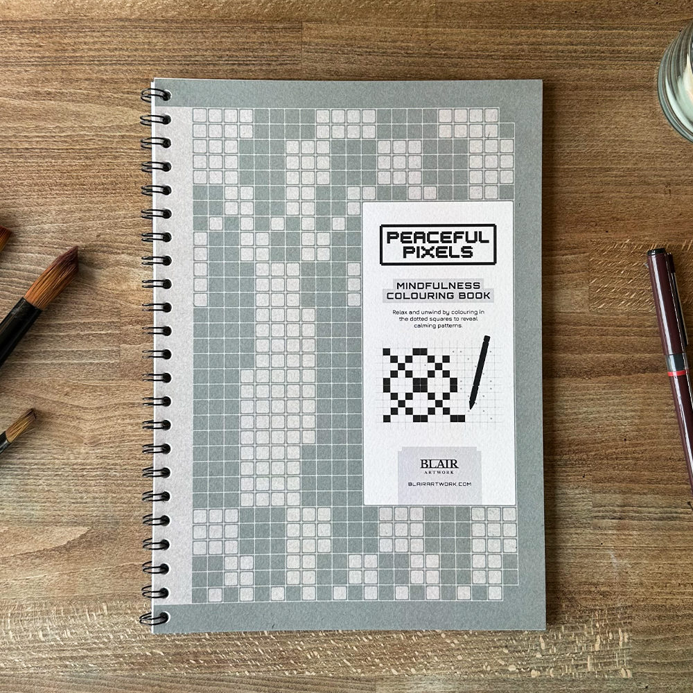Peaceful Pixels mindfulness coloring book on a wooden surface with pens.