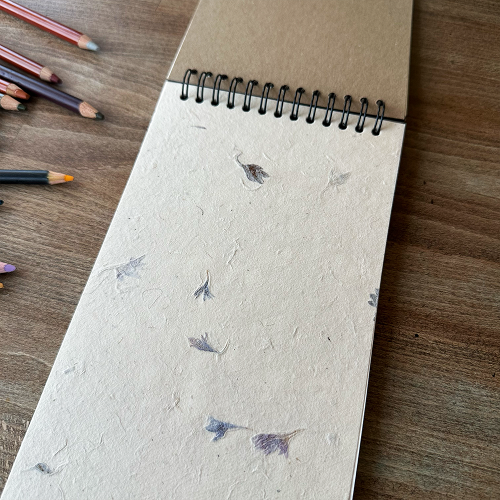 Notebook with floral pattern on a wooden surface with colored pencils.