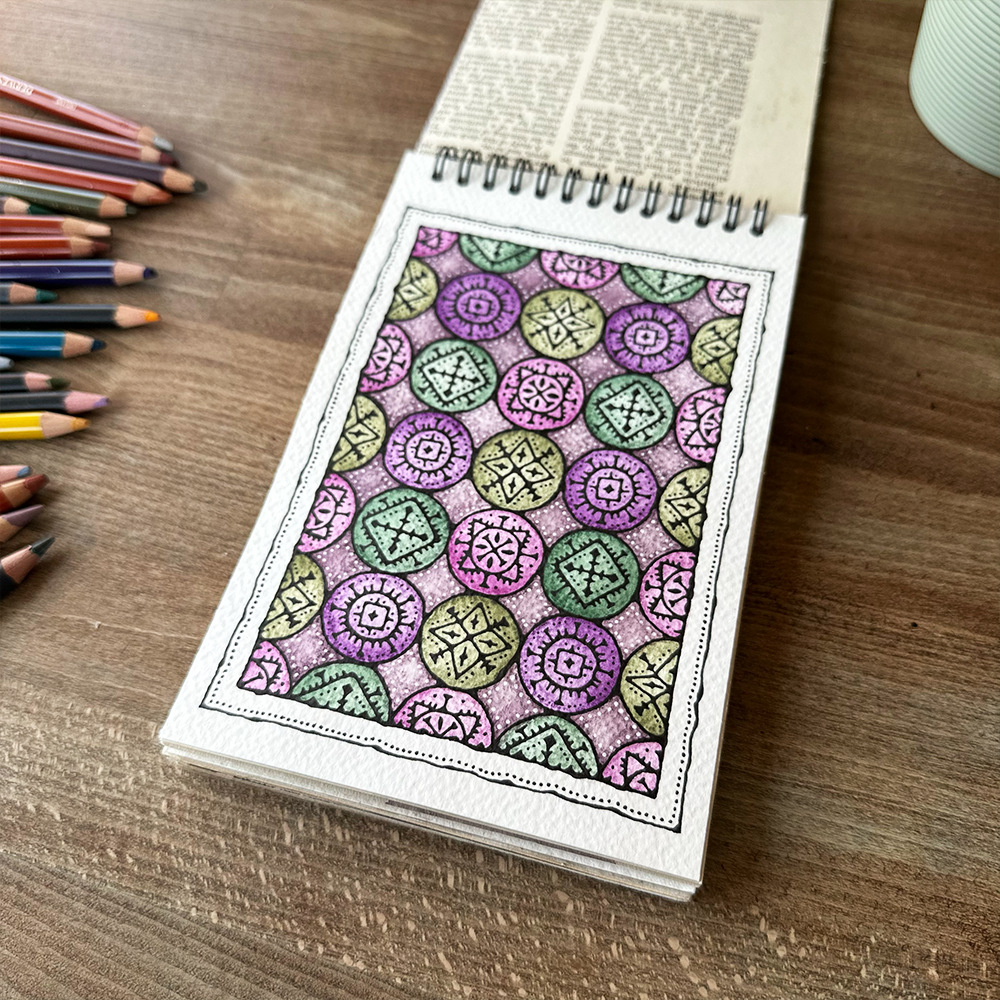 Coloring book with a completed mandala design on a wooden table with colored pencils.
