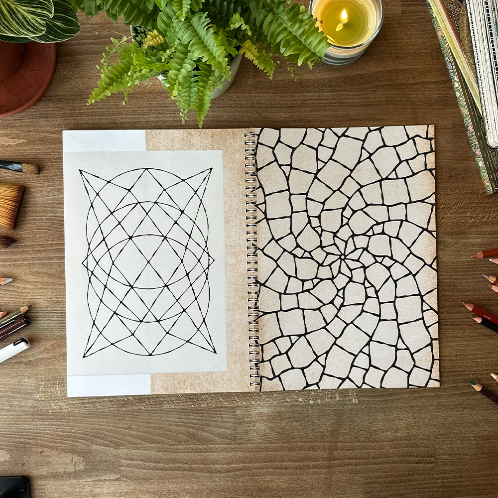 Open notebook with geometric designs on a wooden surface with stationery items.