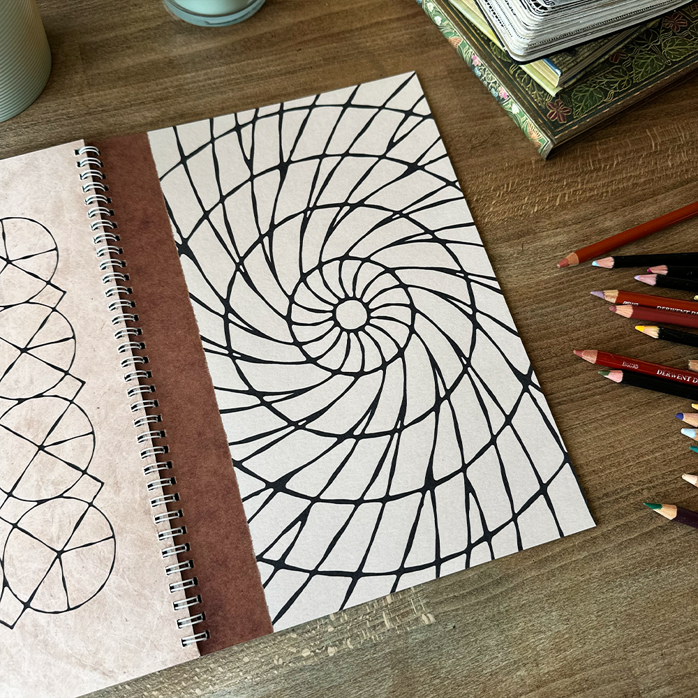 Notebook with geometric pattern on a wooden surface with colored pencils.