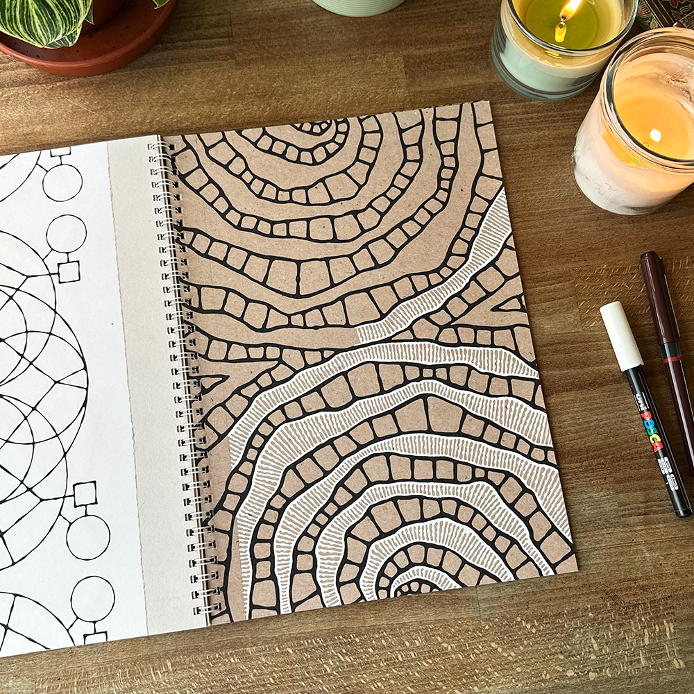 Coloring book with geometric patterns on a wooden surface with candles and markers.