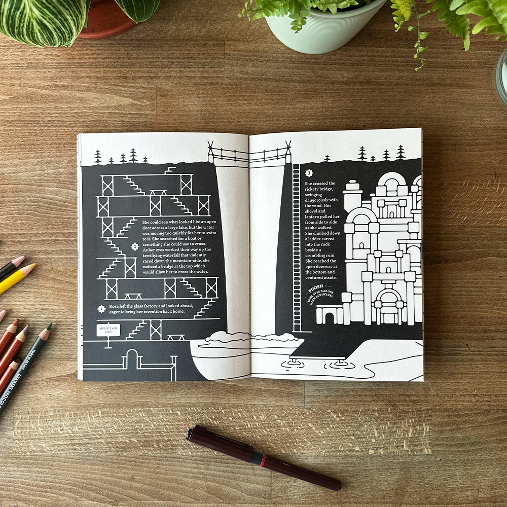 Open book with black and white illustrations on a wooden surface with colored pencils and plants.