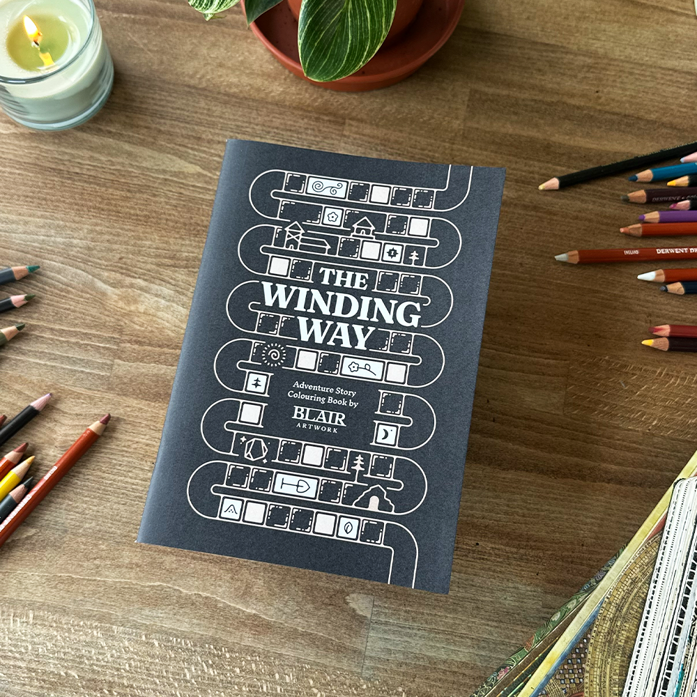 Book titled 'The Winding Way' on a wooden surface with colored pencils and a candle.