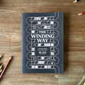 Book titled 'The Winding Way' on a wooden surface with pencils around