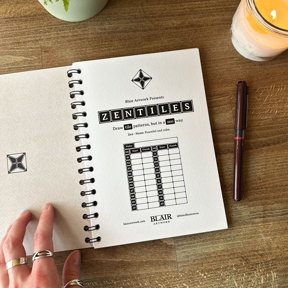 Open notebook with Zentiles design on a wooden table with a pen and candle.