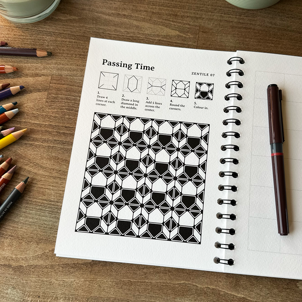 Spiral-bound notebook with a geometric pattern on a wooden surface with art supplies.
