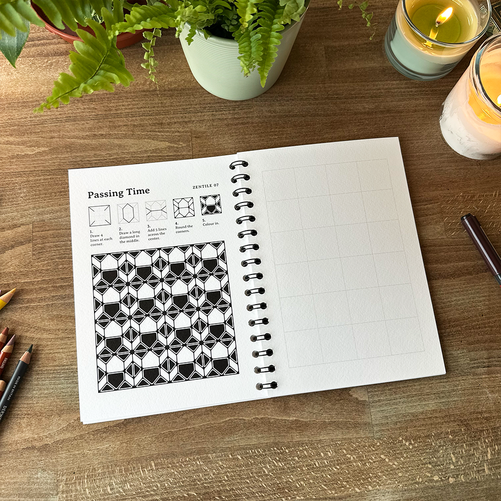 Open notebook with geometric design on a wooden table with candles and plants