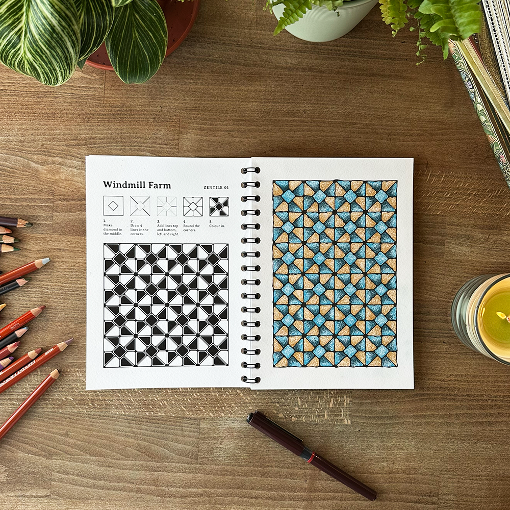 Coloring book with geometric patterns on a wooden table with pencils and a glass.