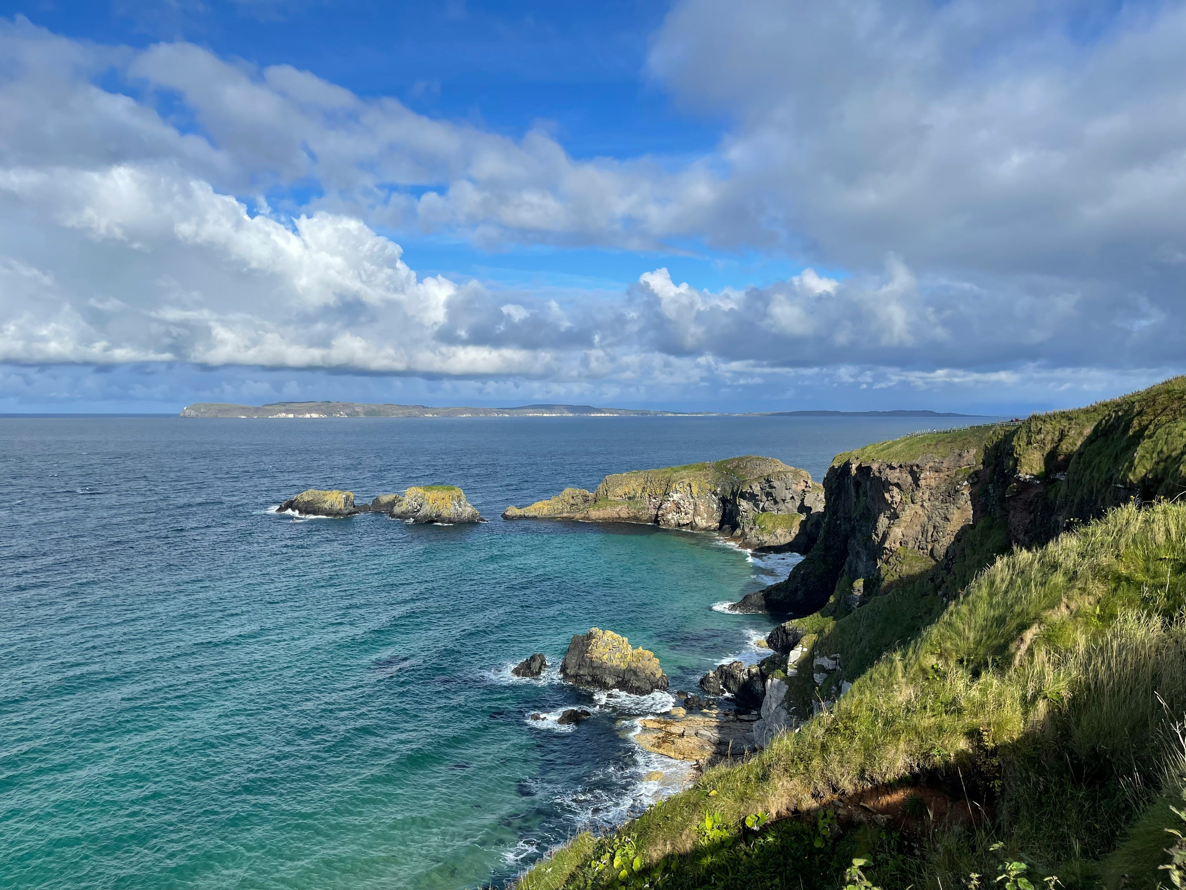 Scenic view of a coastal landscape with cliffs and ocean under a blue sky with clouds.